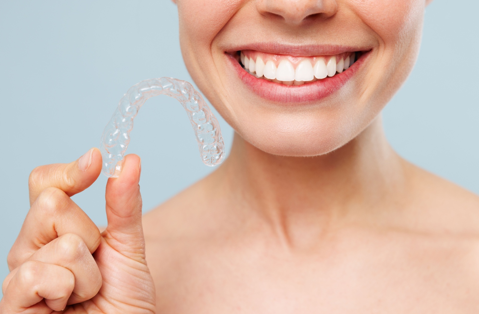 Close-up of a woman smiling while holding a clean Invisalign aligner next to her face.