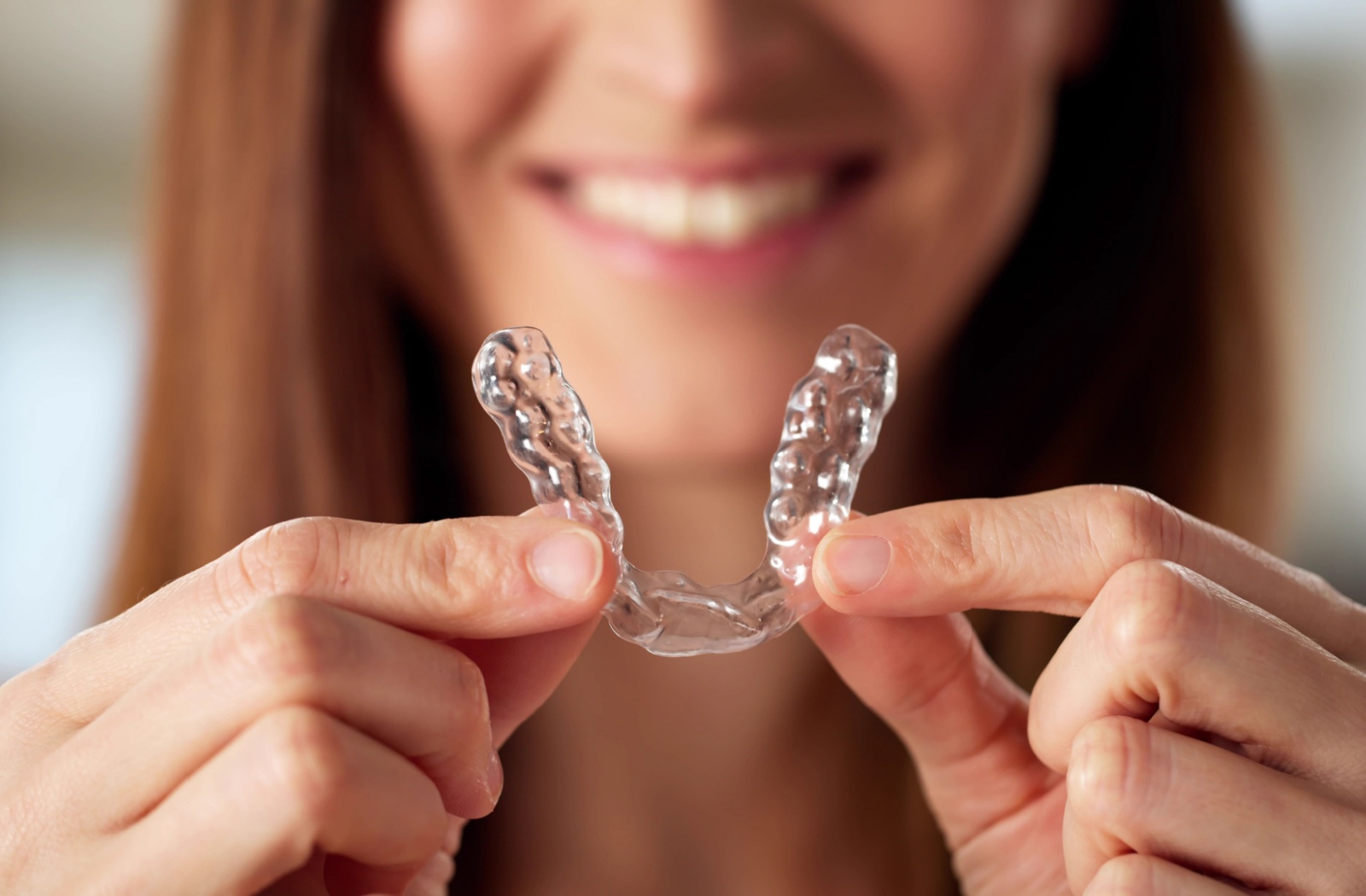 An adult holding up a clear aligner in front of their face